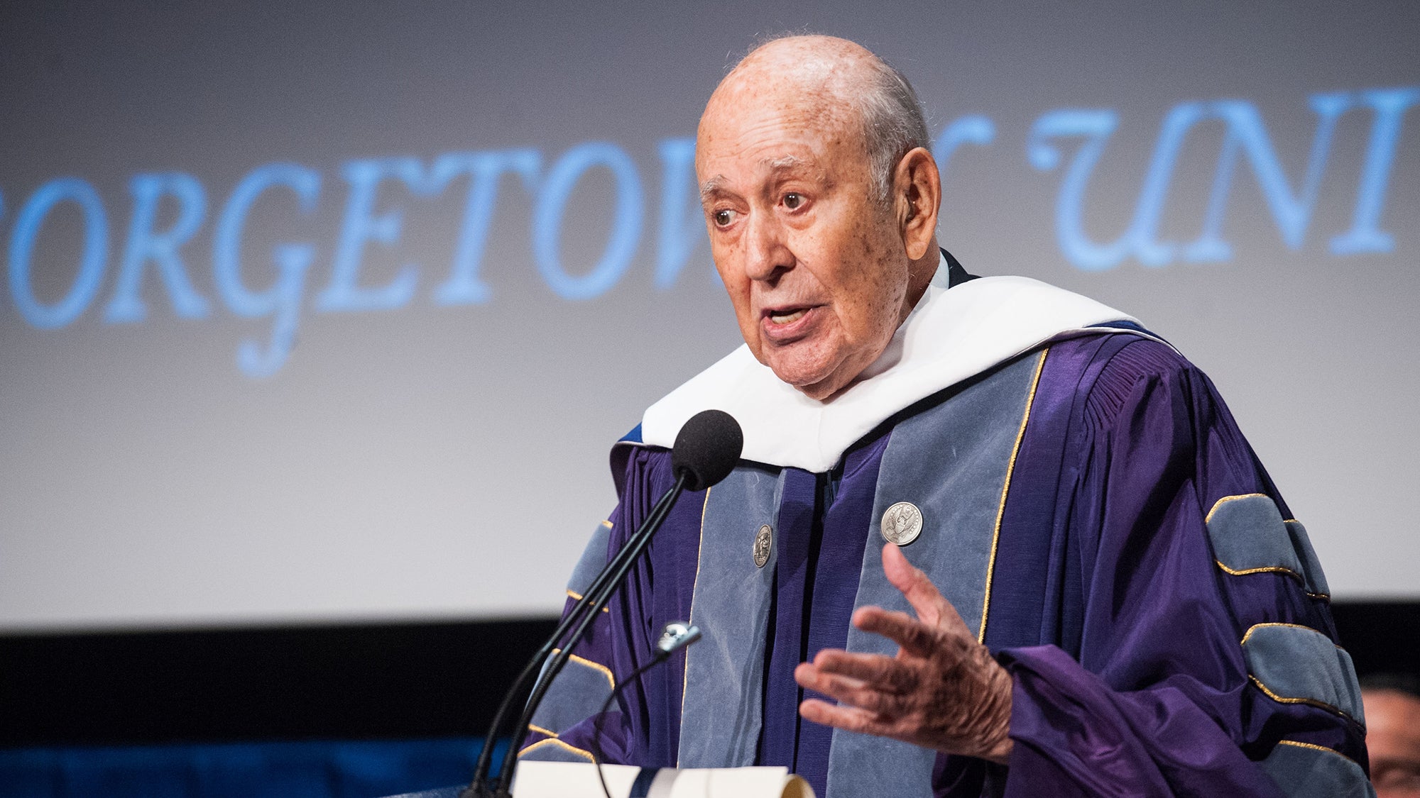 Carl Reiner at a podium wearing academic robs with a screen behind him reading Georgetown University