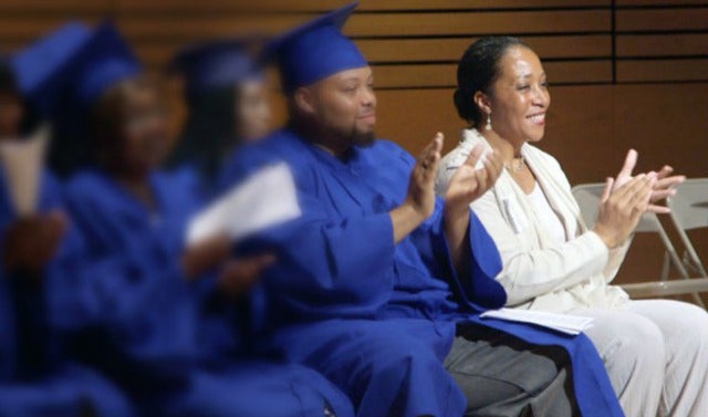 Lecester Johnson sitting and clapping next to students in caps and gowns also clapping