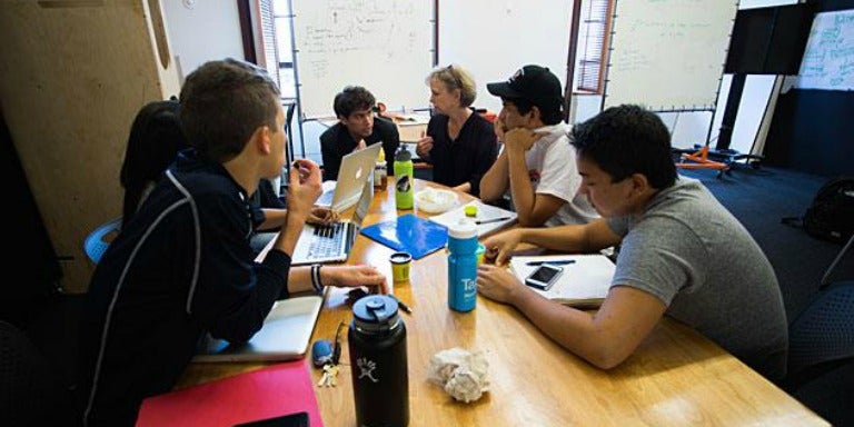 Students sit around a table holding a discussion in the classroom.