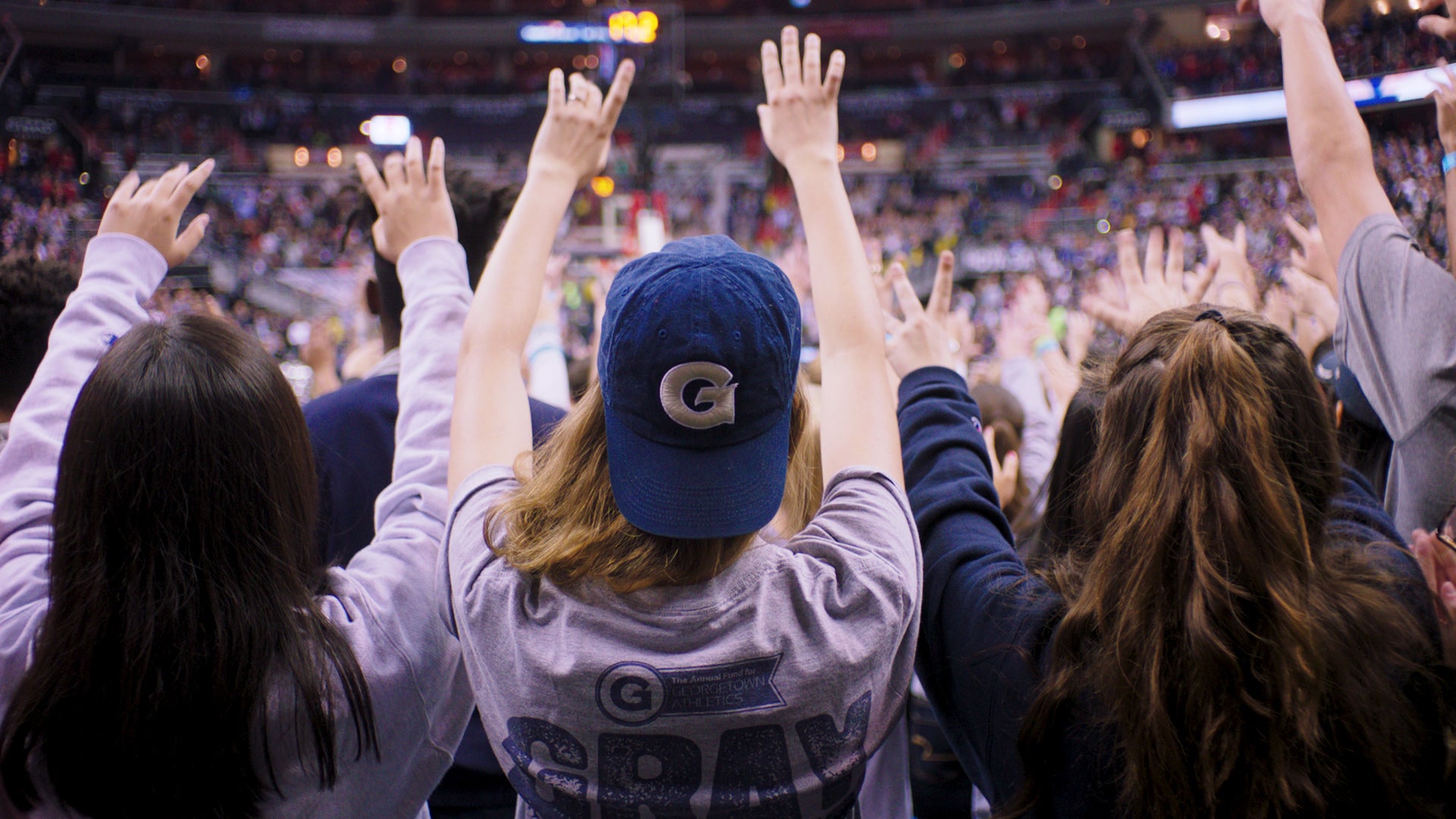 Students are raising their hands in the air at a basketball game.