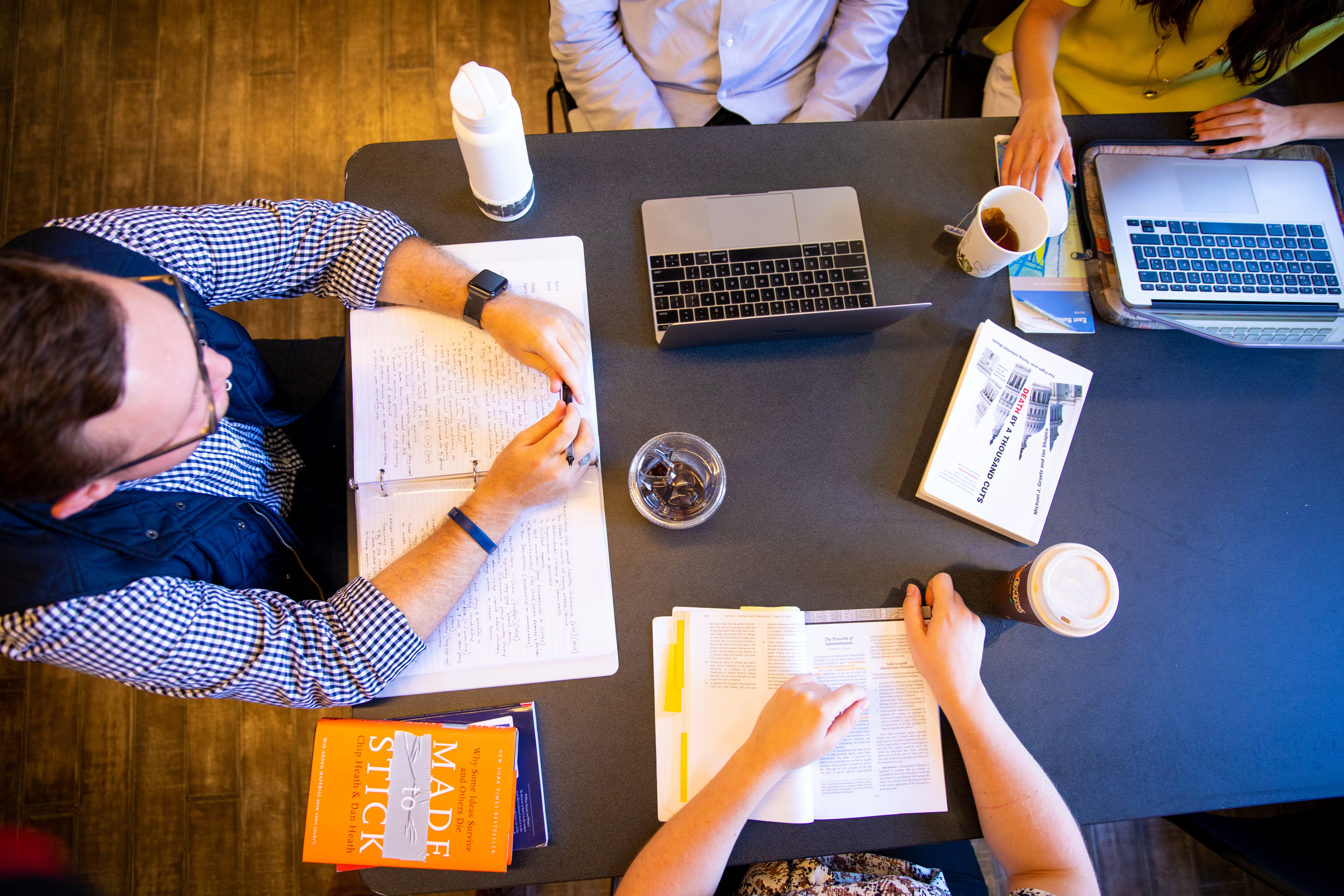 Students are gathered around a table with books and laptops open.