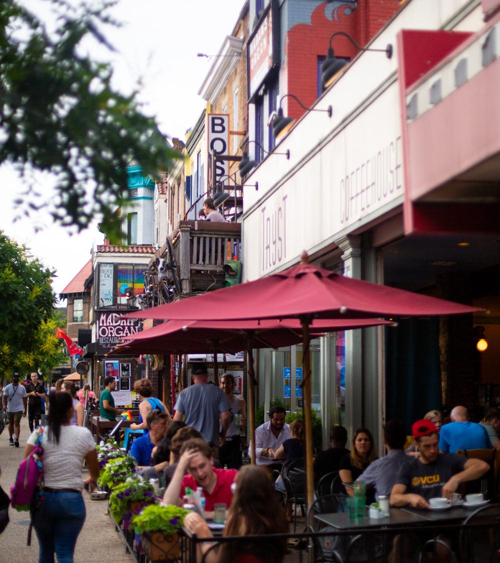 This photo displays a restaurant with sidewalk seating, in which people are seen eating and socializing.