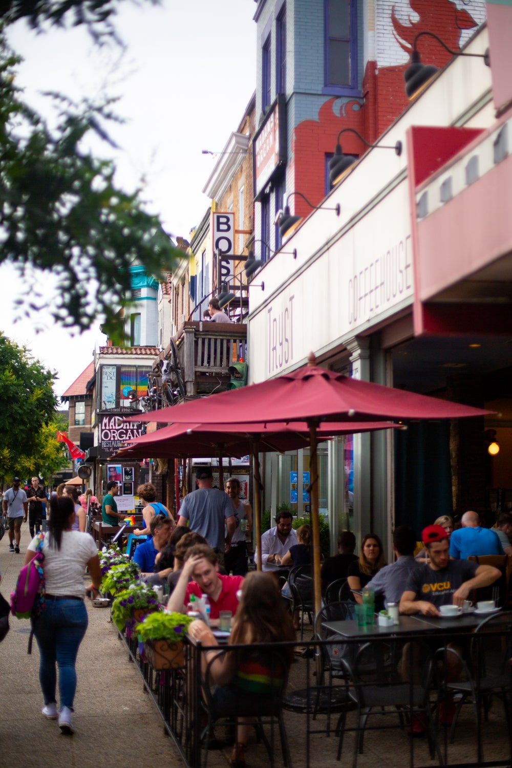 This photo displays a restaurant with sidewalk seating, in which people are seen eating and socializing.