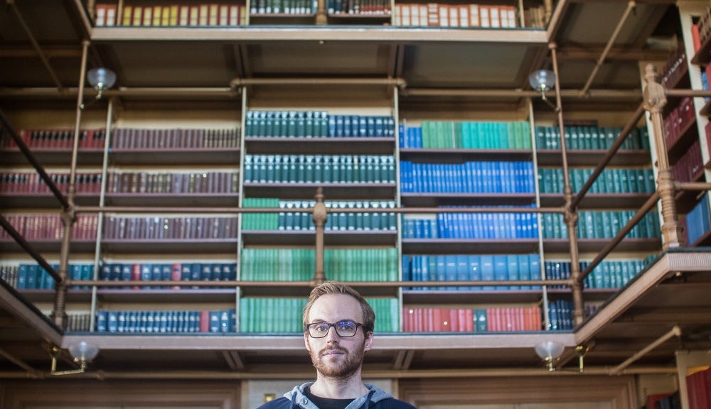 Justin Goss smiles for the camera in a library.