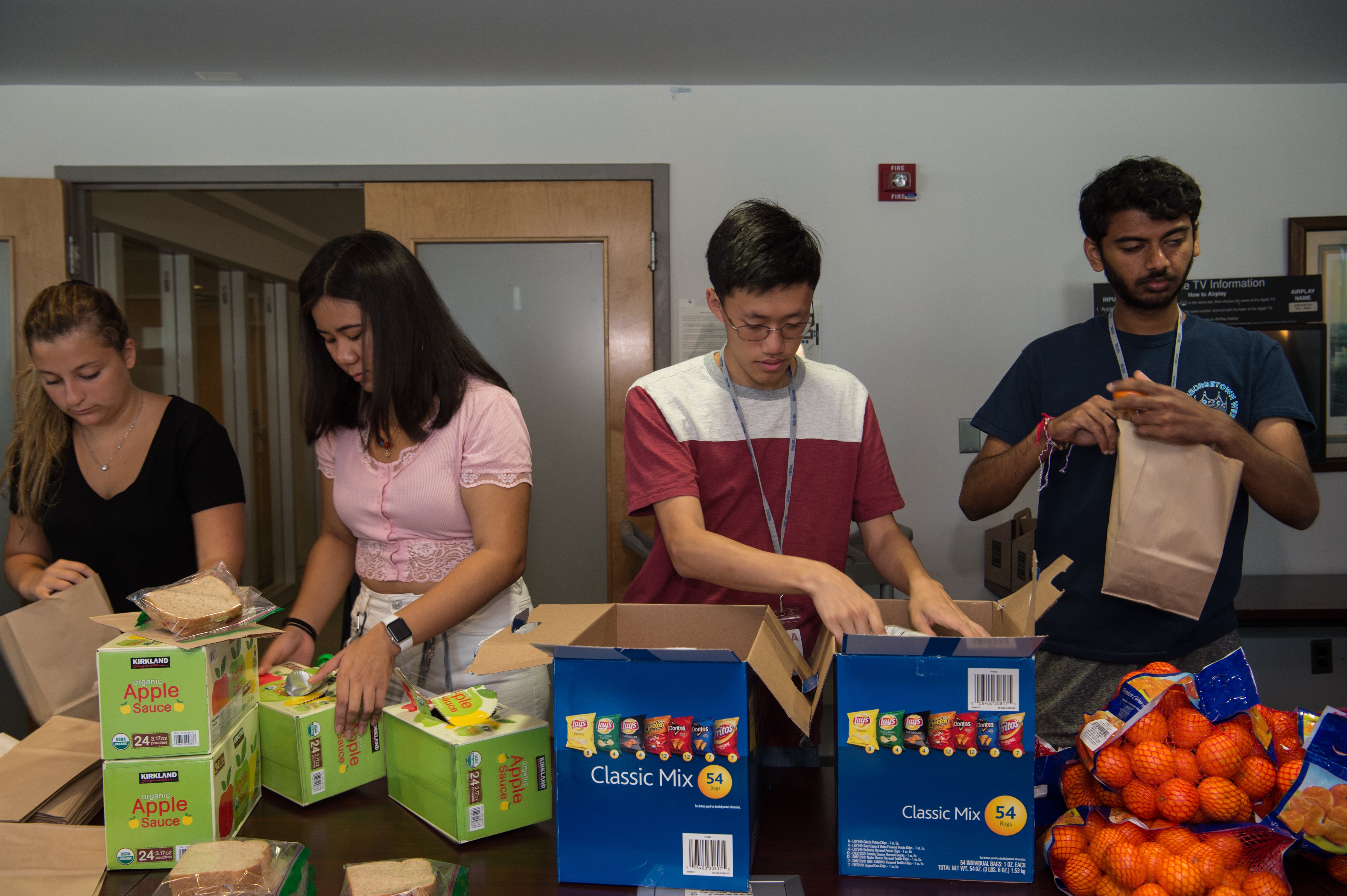 Photo shows four students packing lunch bags in an assembly line.