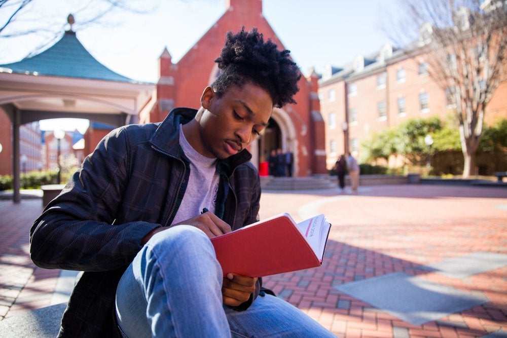 Emmanuel Thomas writes in a notebook while sitting on a bench.