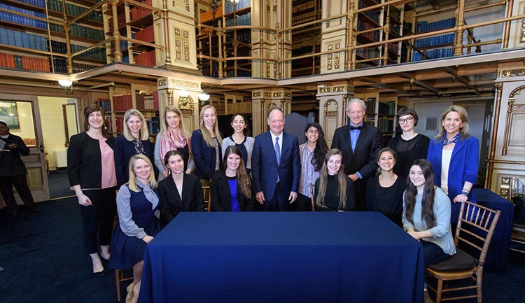 Bill McDonough and John J. DeGioia stand around a table with students and administrators