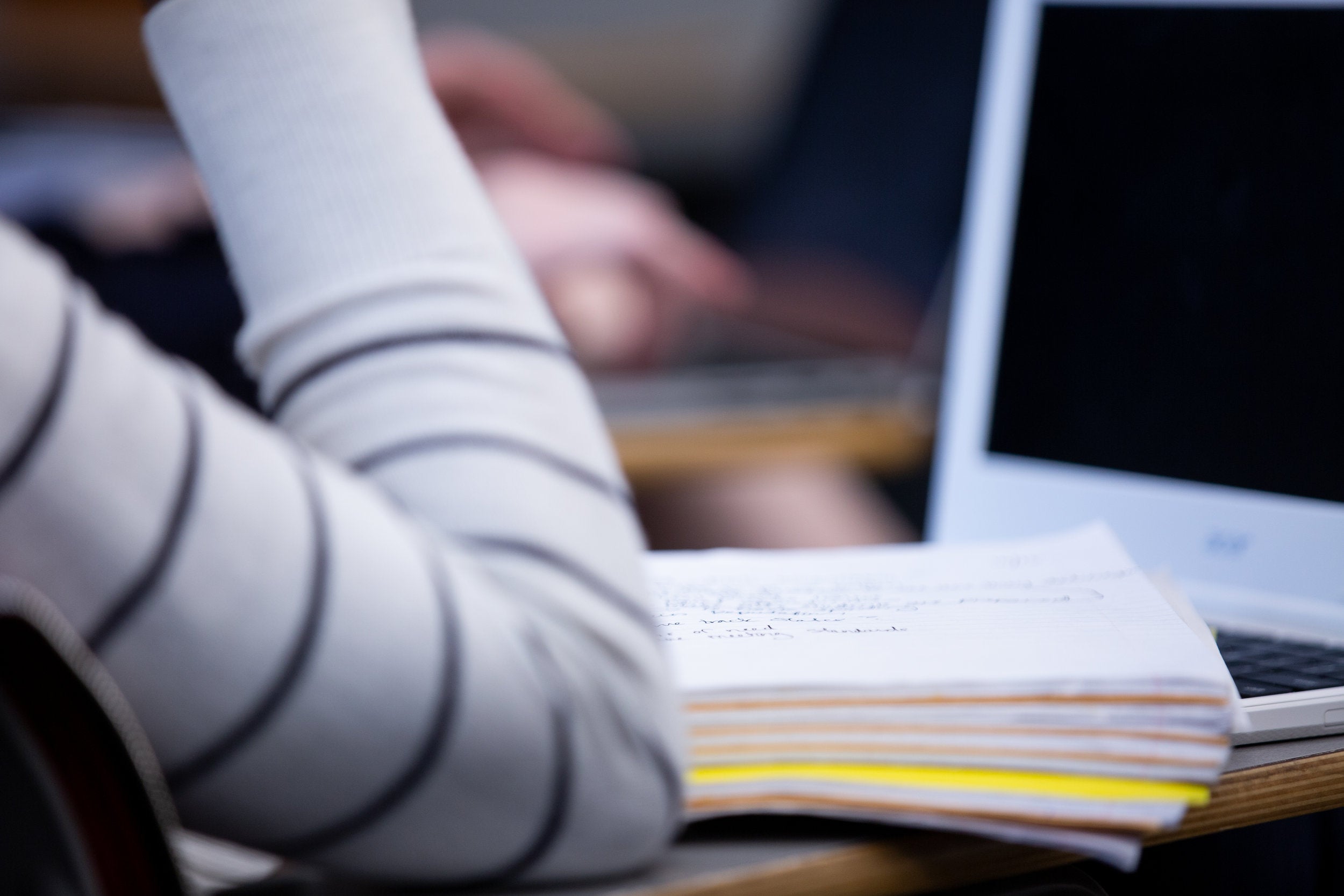 An arm and a notebook resting on a desk.