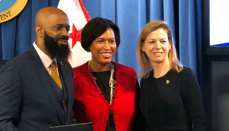 Milford Washington stands to the left of DC Mayor Muriel Bowser and Kelly Otter stands to the right.