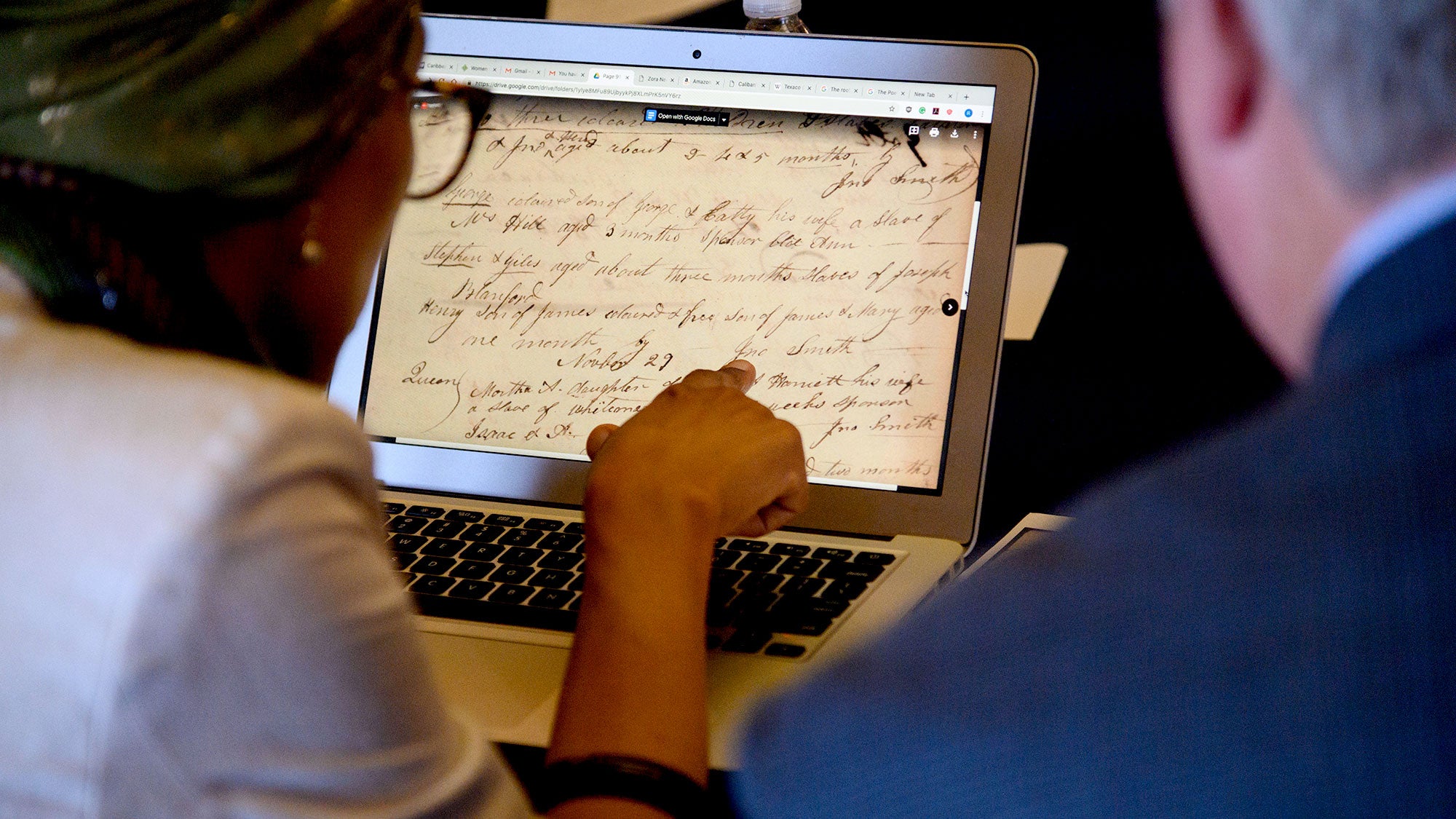 A woman and a man look at historical documents on a latop screen.