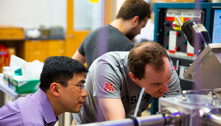 Georgetown physics professor Kai Liu and two graduate students work with equipment in a lab.