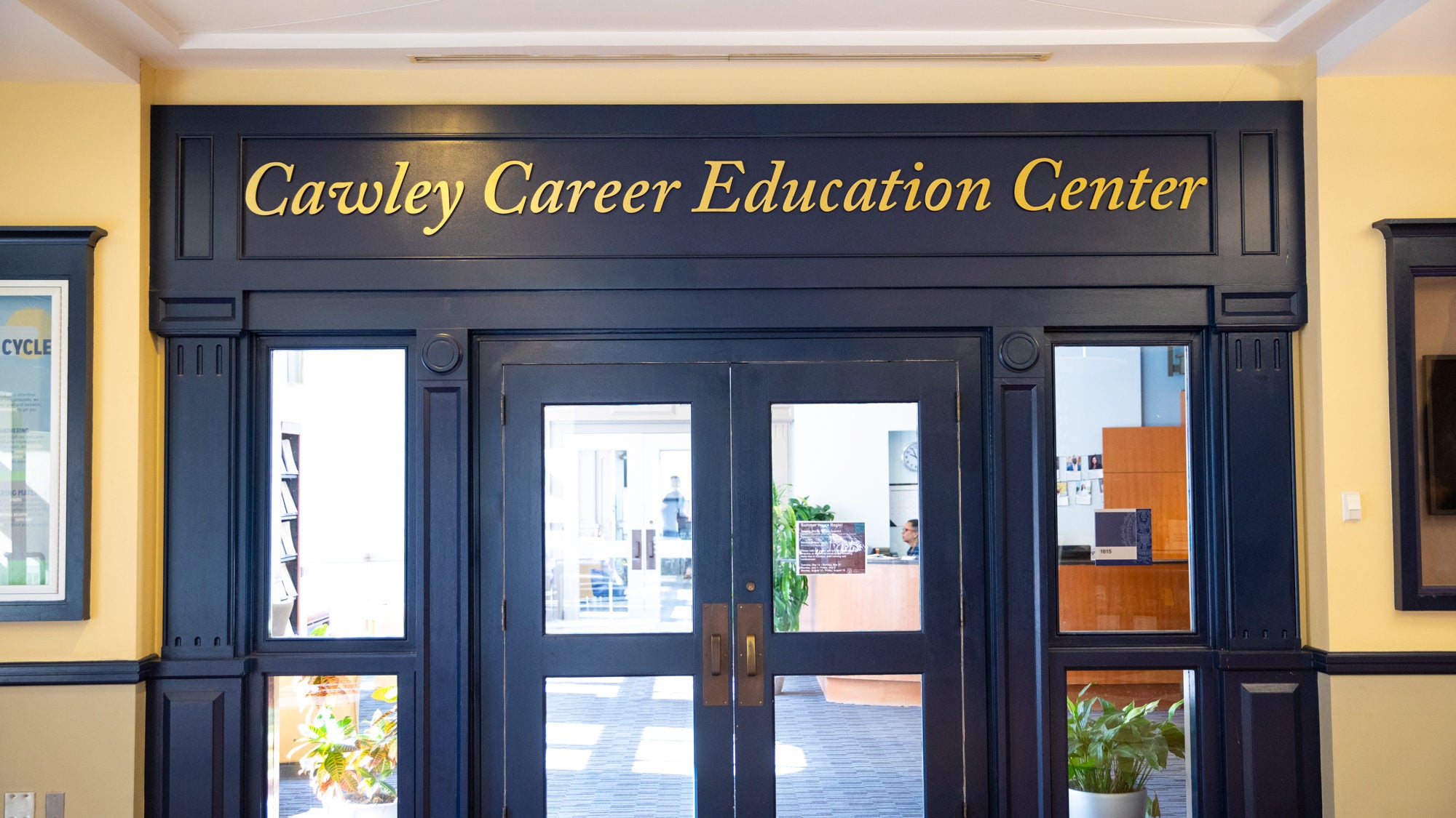 The words &quot;Cawley Career Education Center&quot; are engrained in gold letters above a set of glass doors with navy blue frames.