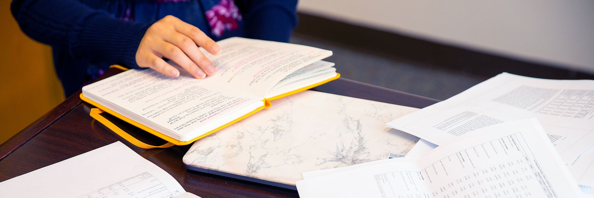 Person's hand over an open book with notes