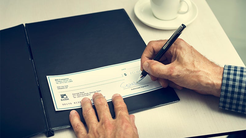 an older man's hands, one of which is writing a check