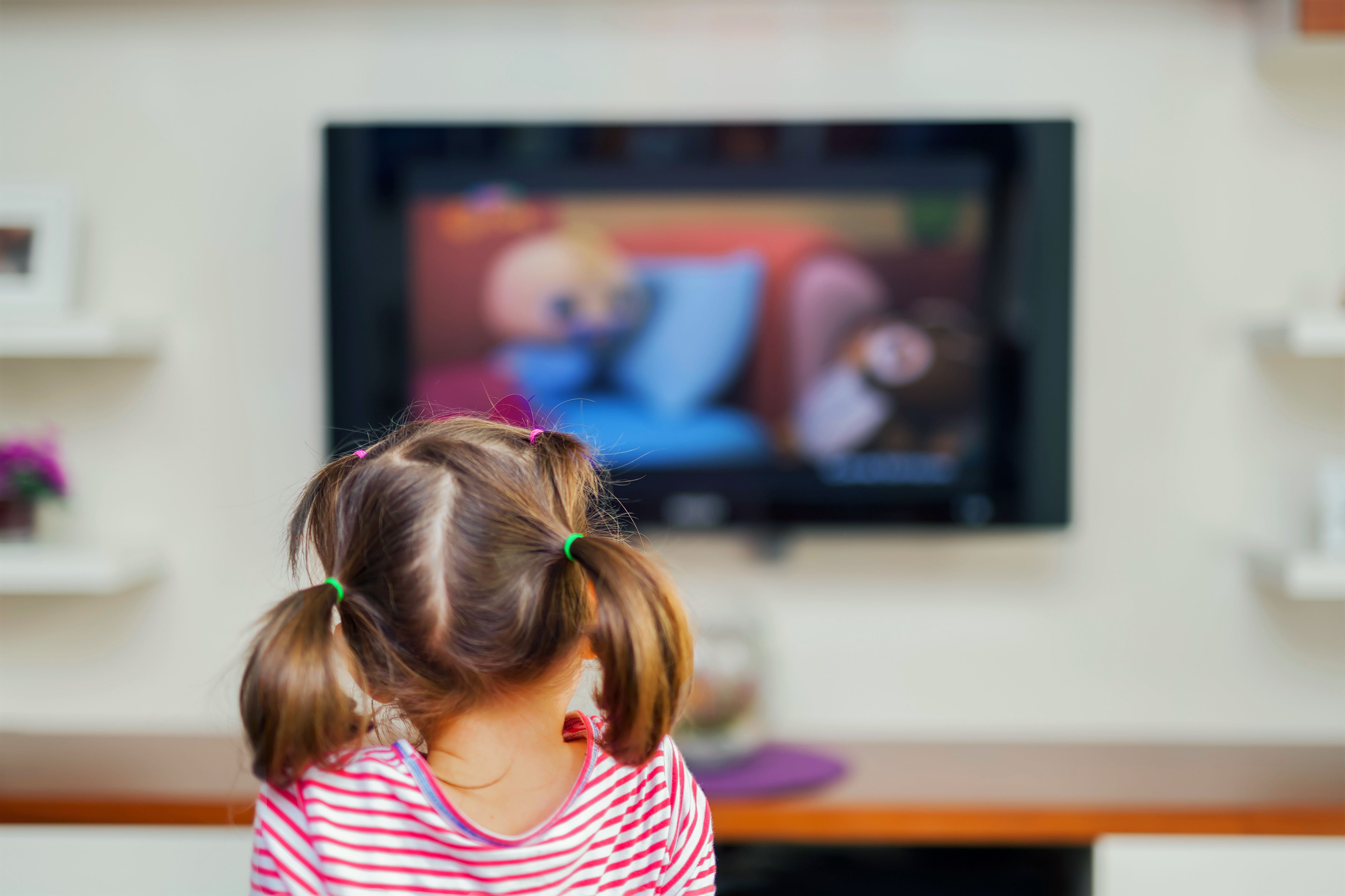 A little girl facing a TV showing a children's program