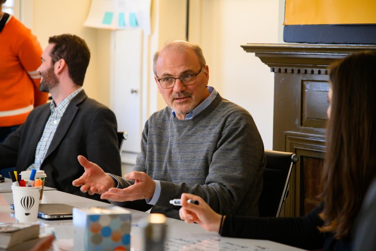 Randy Bass gestures at a table with two people sitting next to him