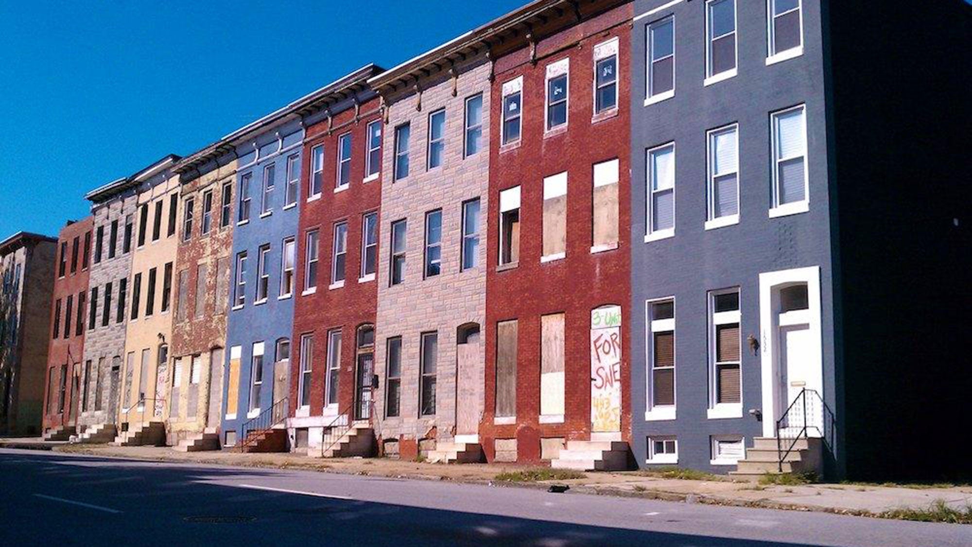 Five colorful, abandoned rowhomes stand side-by-side along a quiet street.