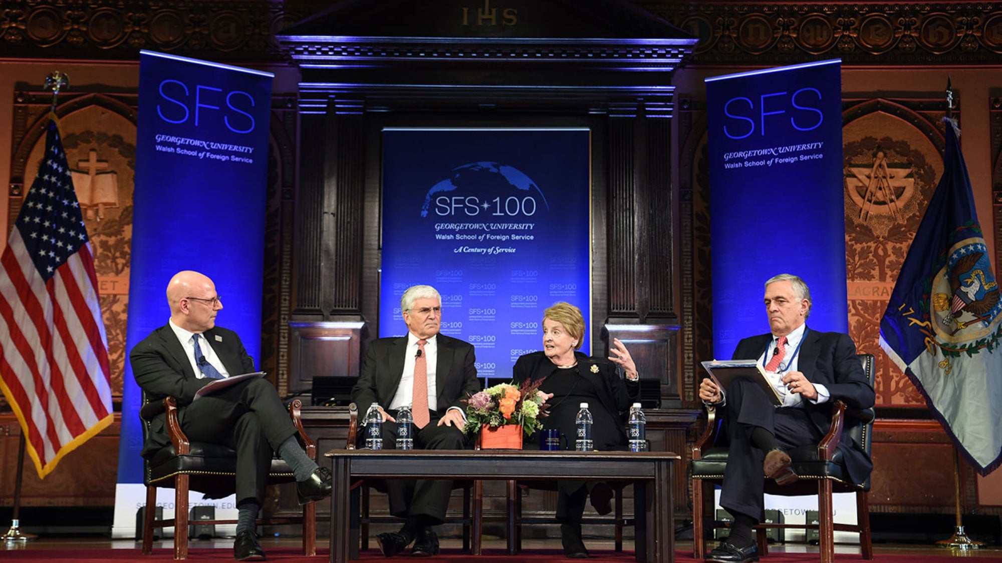 Joel Hellman, George Casey, Madeleine Albright and George Tenet sit on stage in Gaston Hall with blue SFS 100 banners in the background.