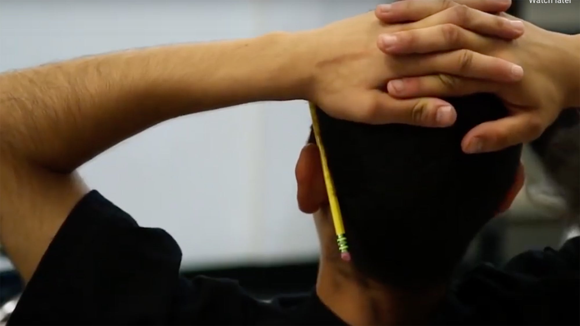 A young man with his hands folded on top of his head and a pencil behind his ear