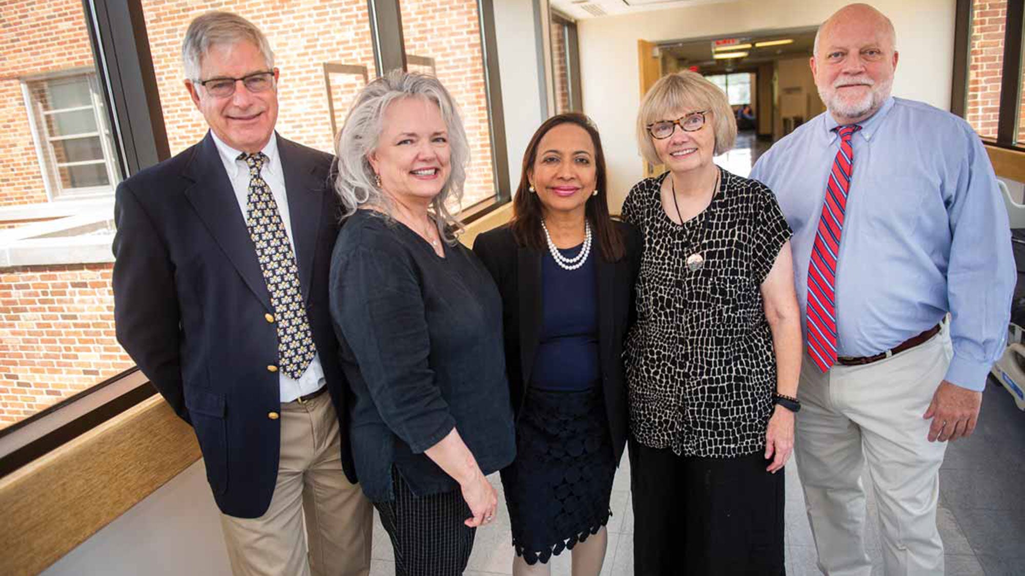 Phil Pierce, Ella Curry, Princy Kumar, Mary Young and Chip Read stand together near windows in a building.