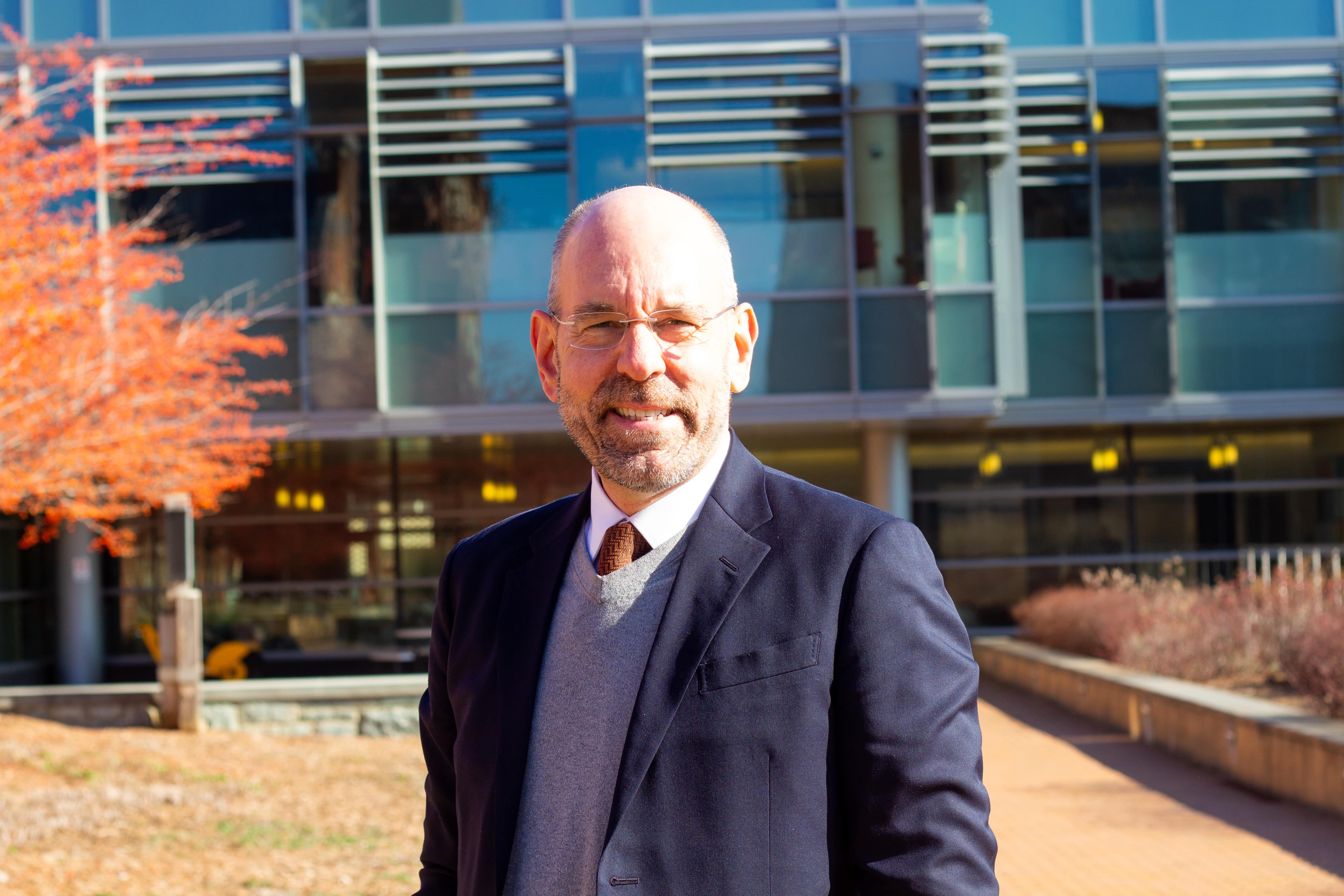 Professor Brandes stands in front of the Regents Building smiling