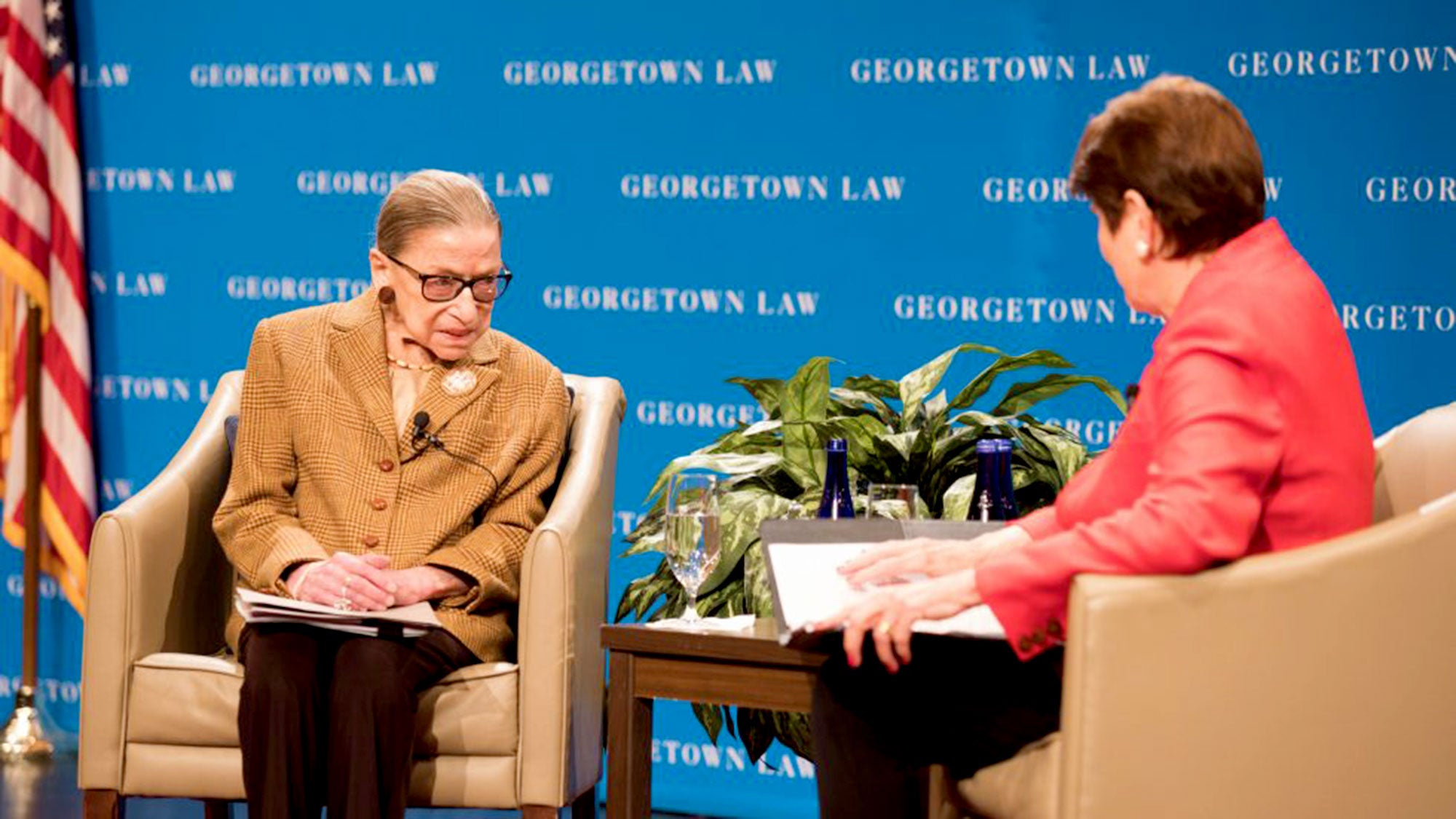 Ruth Bader Ginsburg sits on stage talking to M. Margaret McKeown with blue Georgetown Law signage in the background.