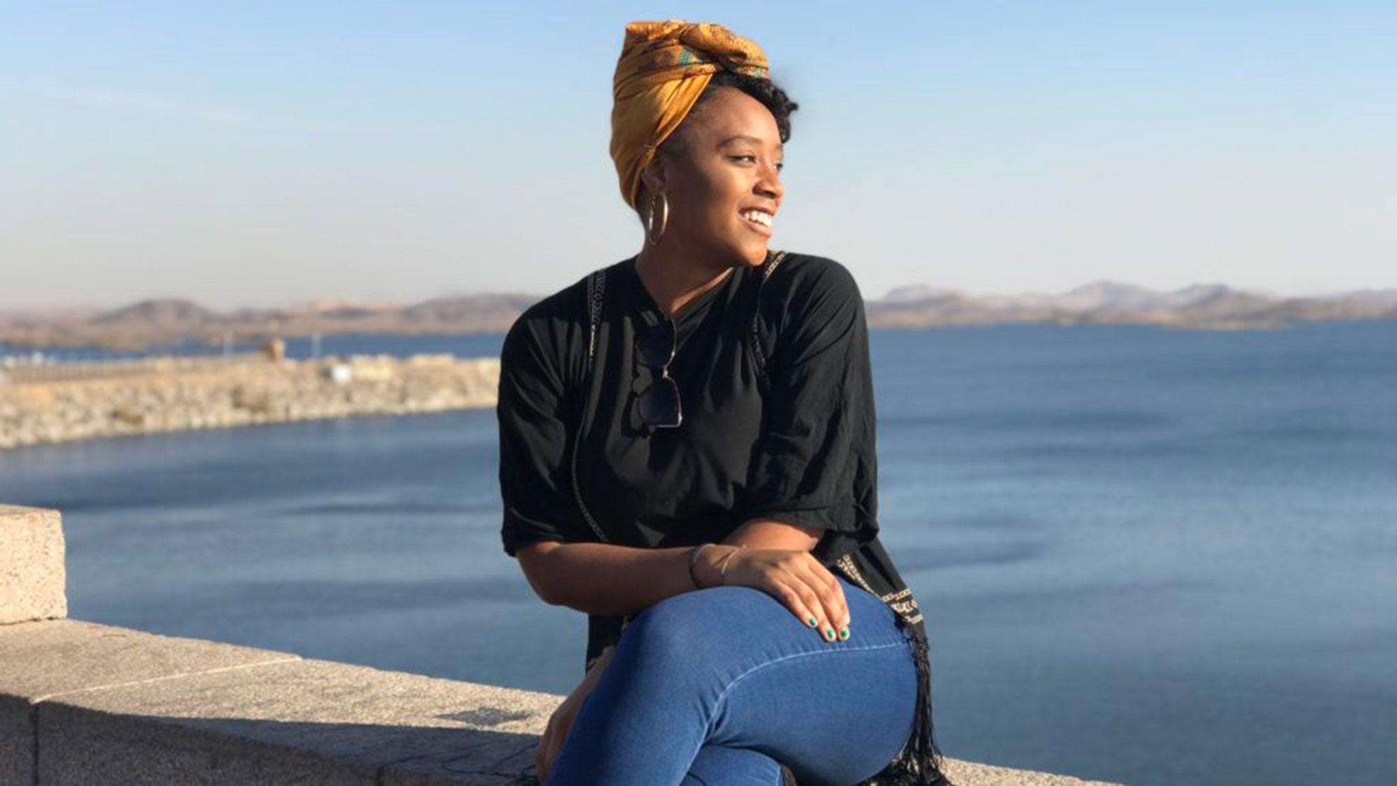 Jada Bullen sits on a wall along the coast with a body of water in the background.