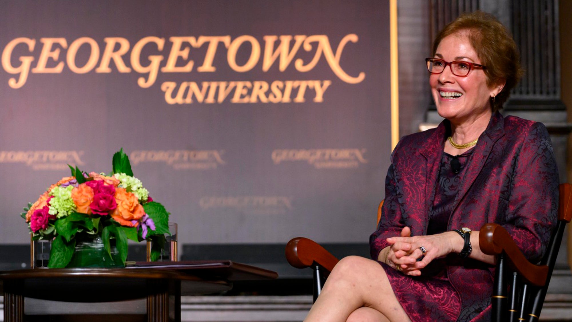 Marie Yovanovitch sits on a stage with her legs crossed in front of a Georgetown banner