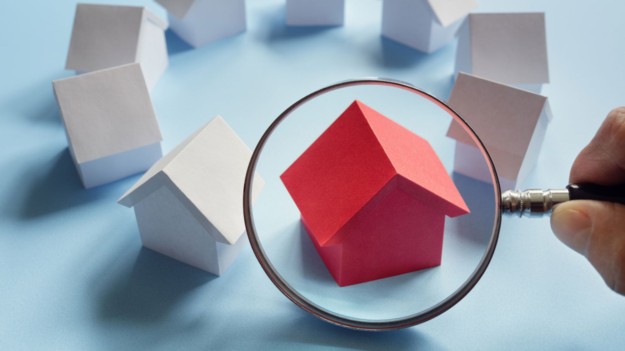 An illustration of little white houses in a circle with a magnifying glass focused on a red house in the circle.