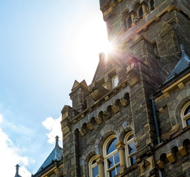 The sun peeks out from the corner of an opening between Healy Hall and the sky.