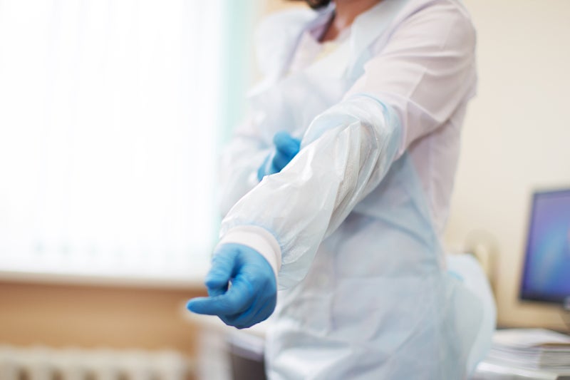 A health professional wearing gloves pulls on a protective gown