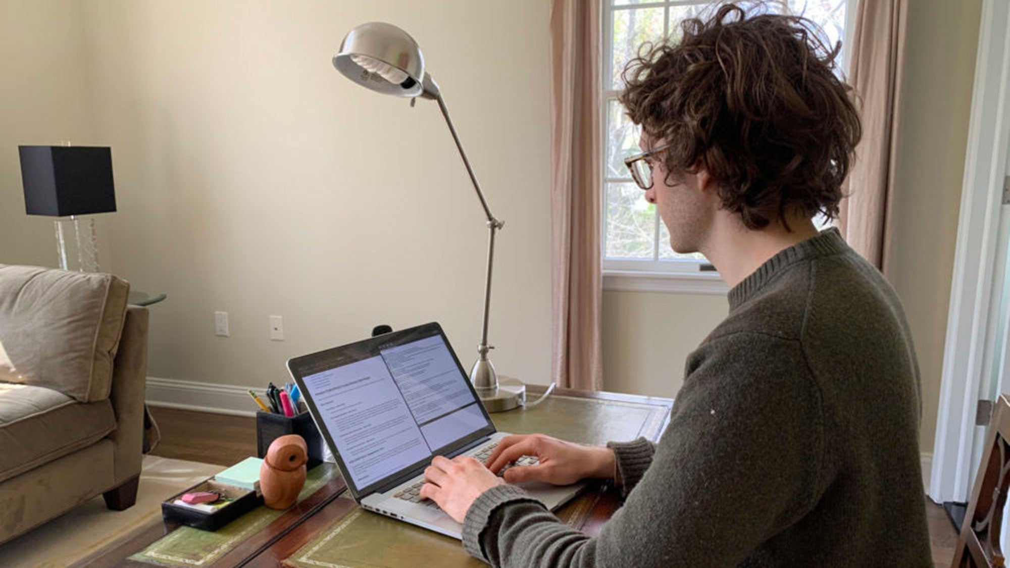 Adrian Hertel sits at a desk typing on his laptop.