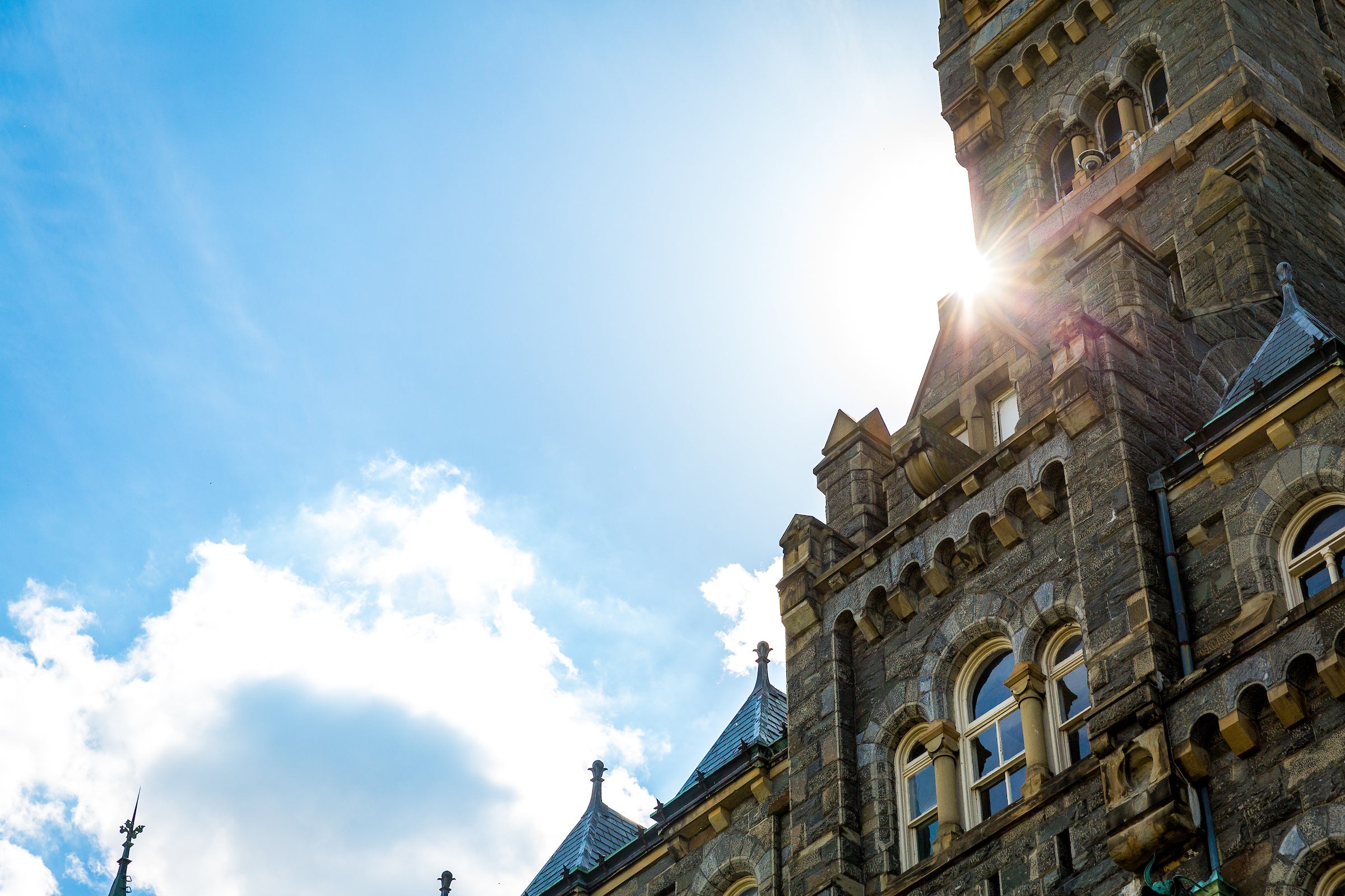 The sun flares from behind the Healy Hall clock tower