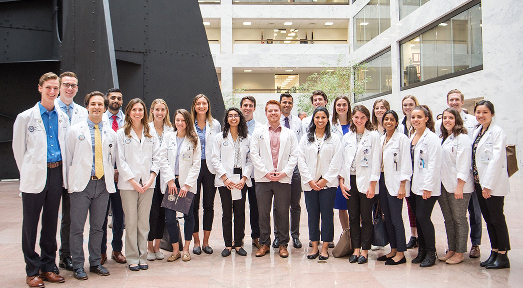 A group of medical students stand together wearing white coats.