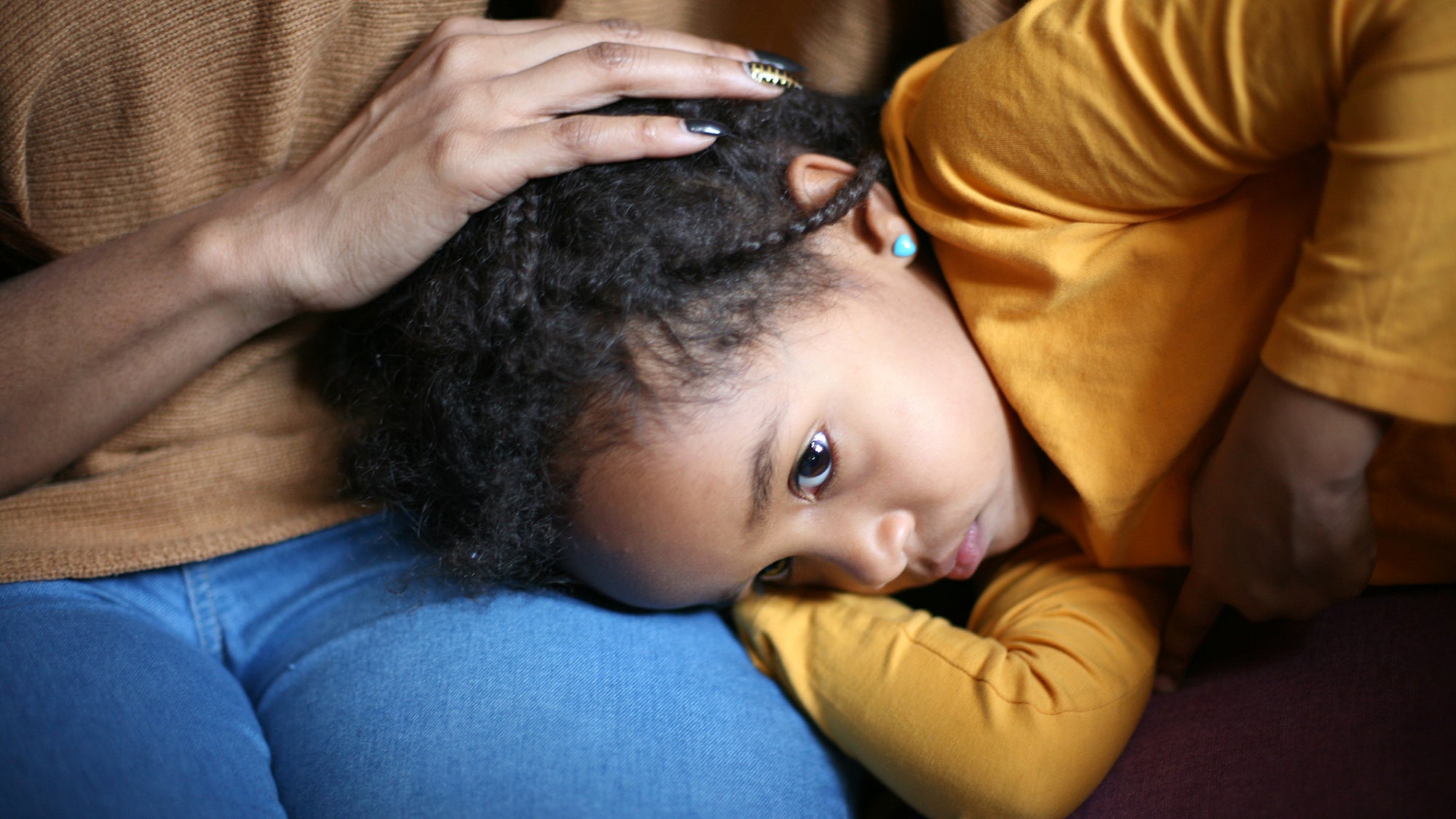 Child with her head on her mother's lap showing just the mother's hand on the girl's head