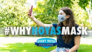 A student takes a selfie with a mask on with text that says "#WhyHoyasMask"