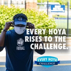 A student puts on a mask with the text "Every Hoya Rises to the Challenge."