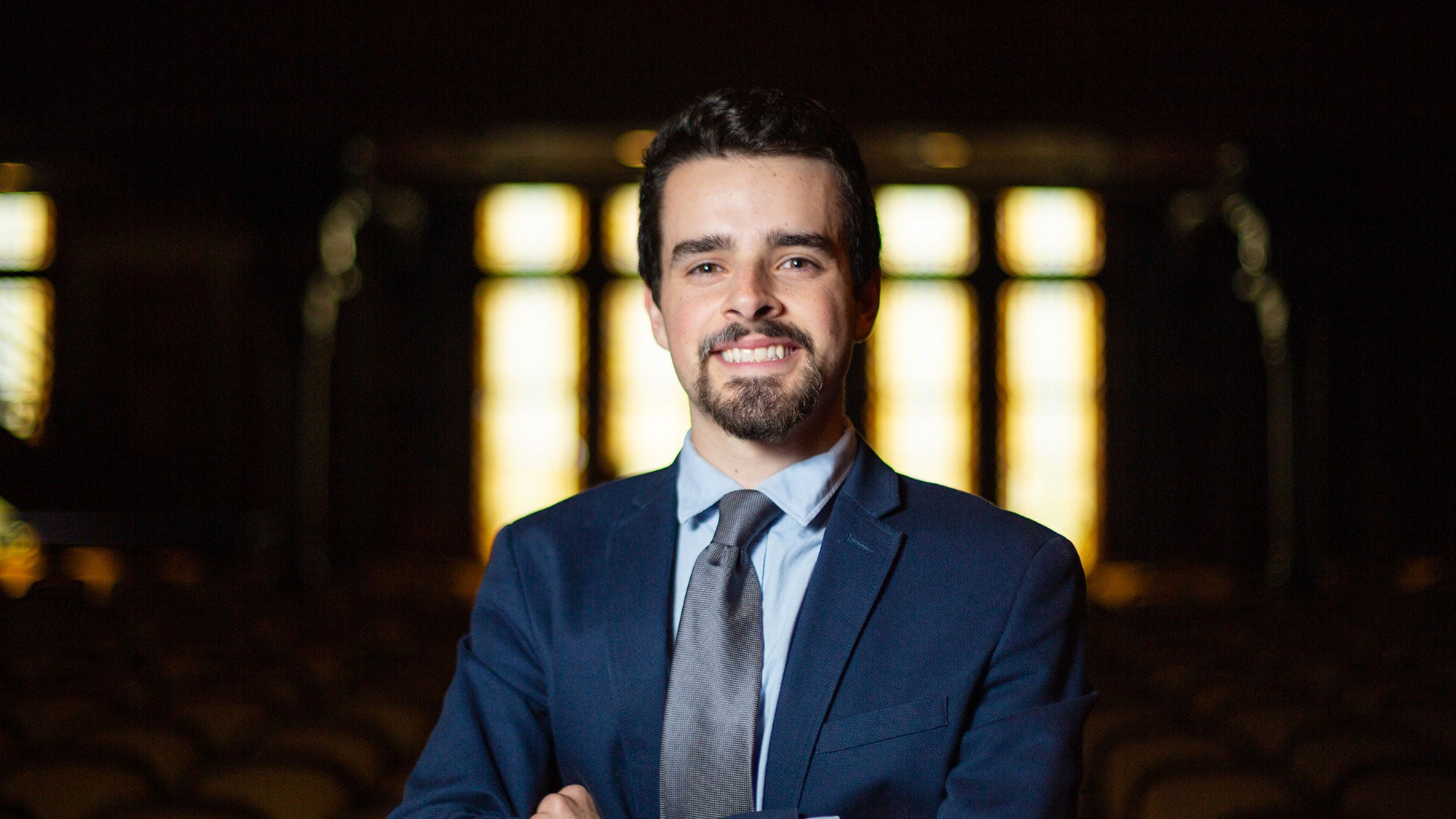 Robert Cortes Stands in Gaston Hall with arms folded.