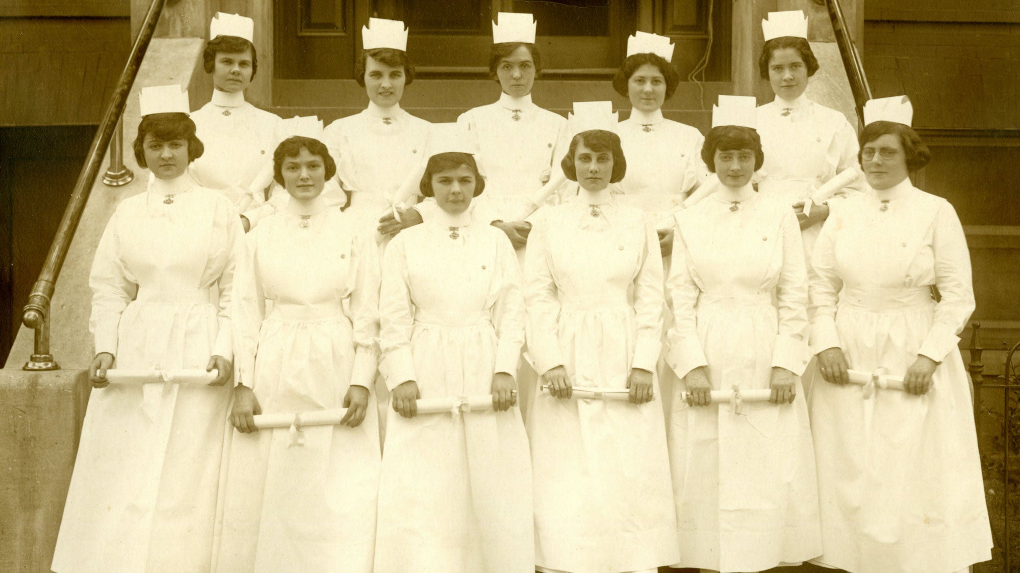 Eleven nurses stand in two rows on steps dressed on uniform in a 1920 photo.