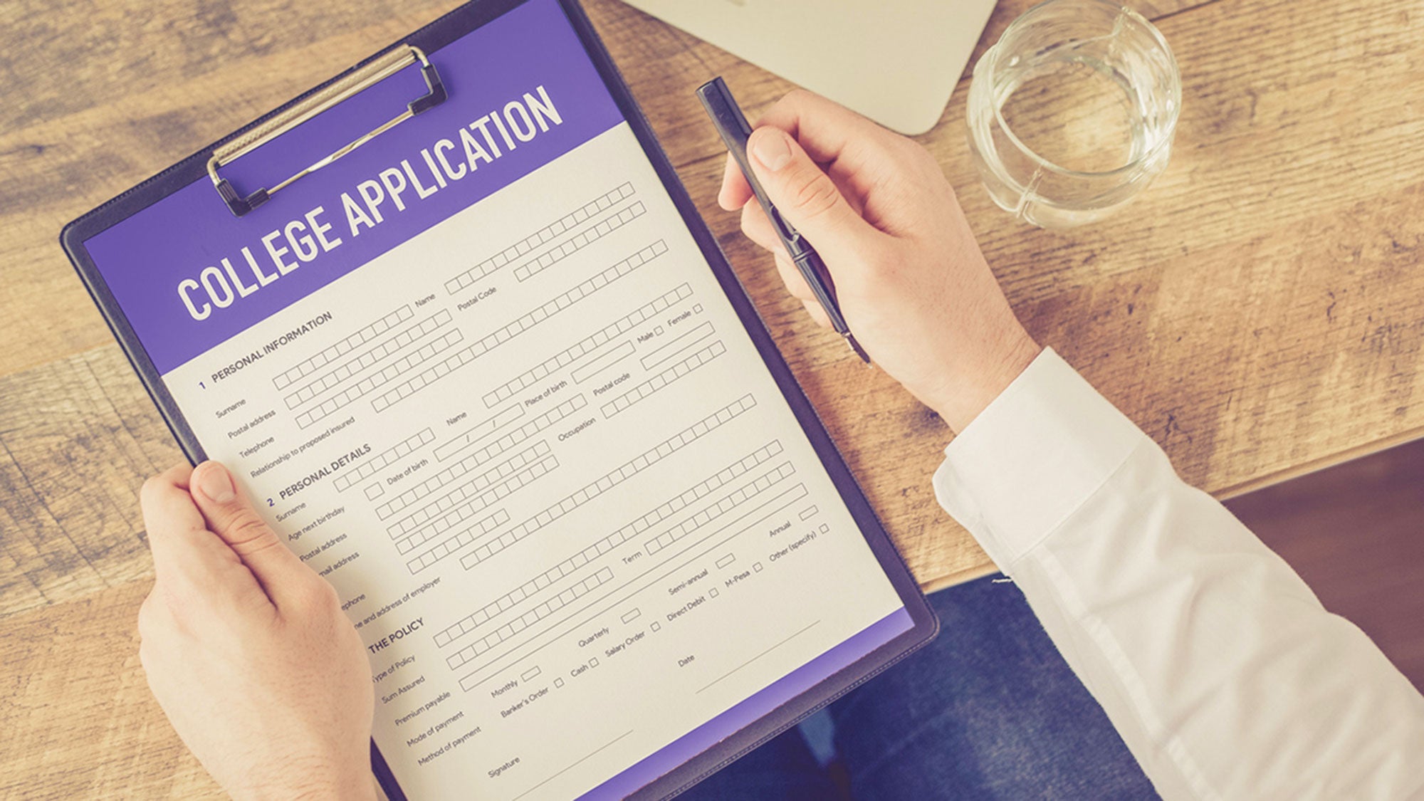 A person holds a pen ready to fill out a college application.