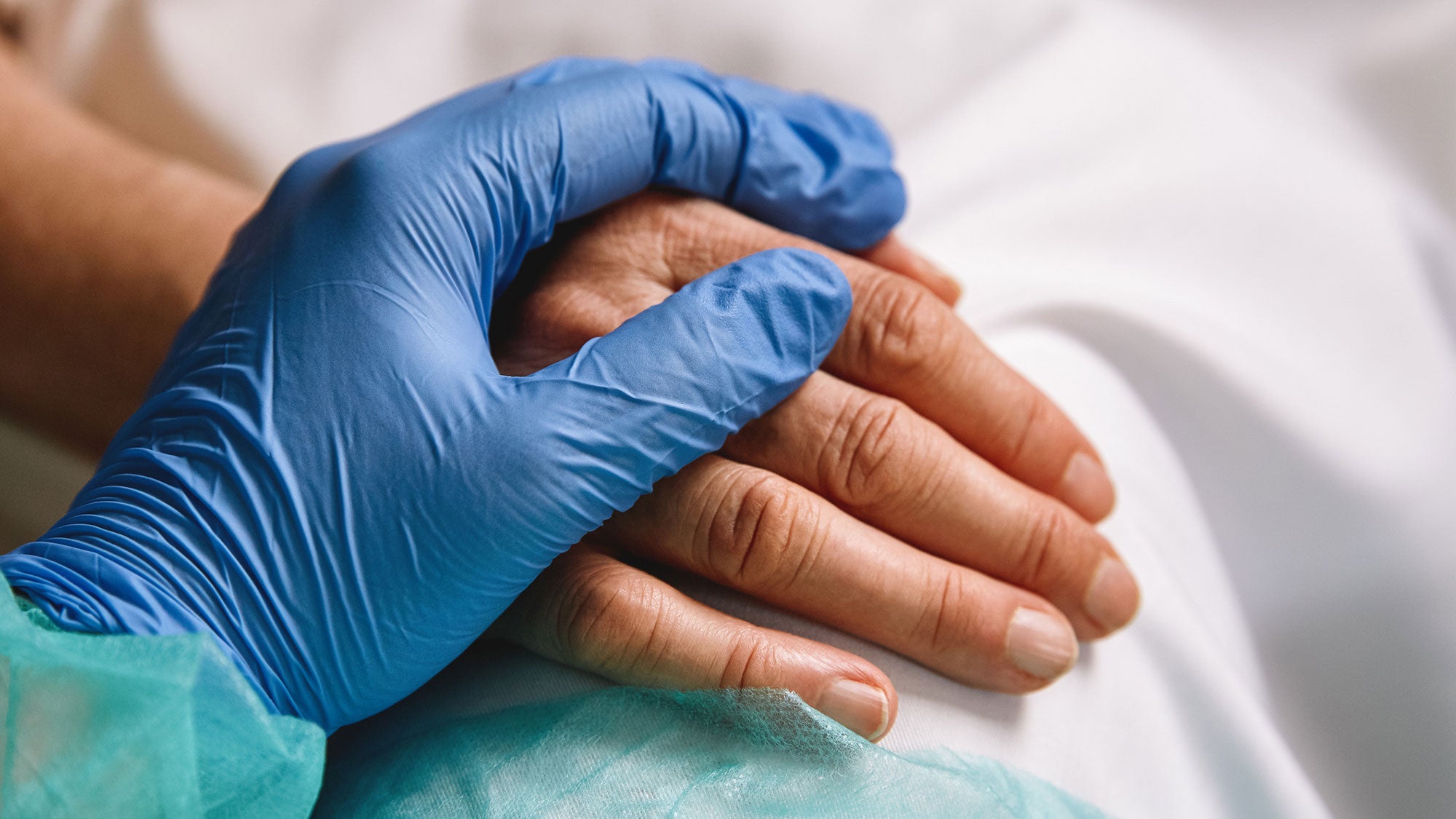 The hand of a gloved health worker rests on top of a patient's hand.