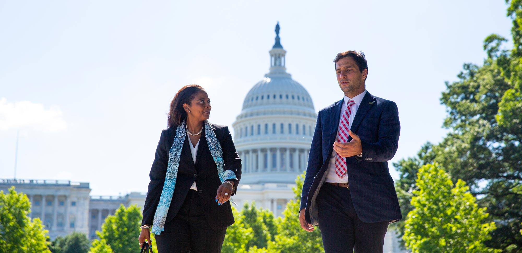 Woman and man in business clothes walk in front of the Capitol Building