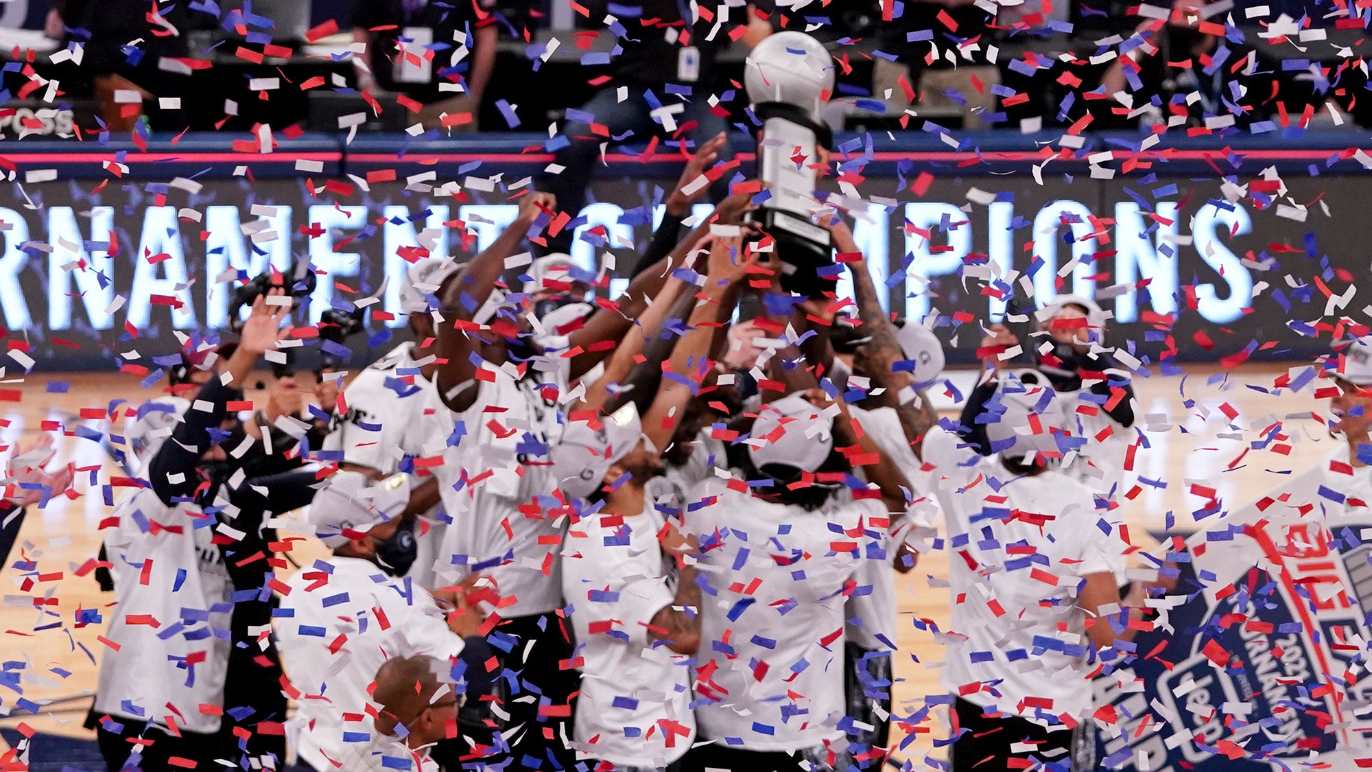 The men's basketball team celebrate on the court after winning the BIG EAST championship as confetti falls.