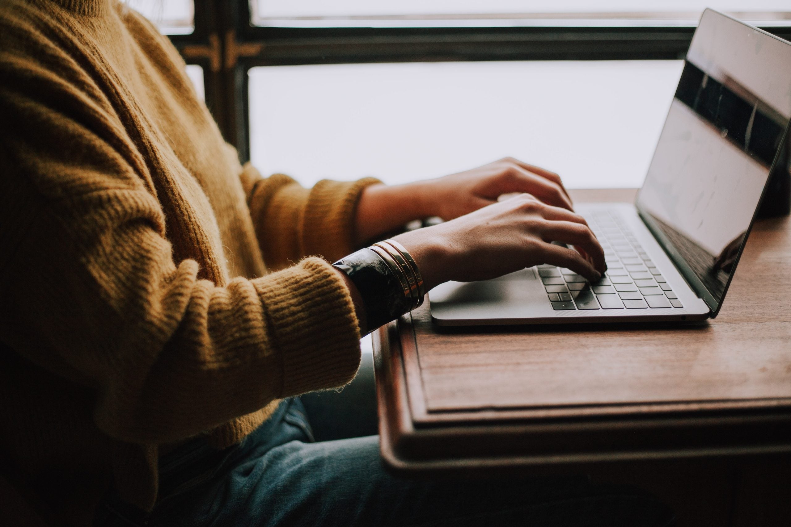 Woman wearing an orange sweater types on a laptop