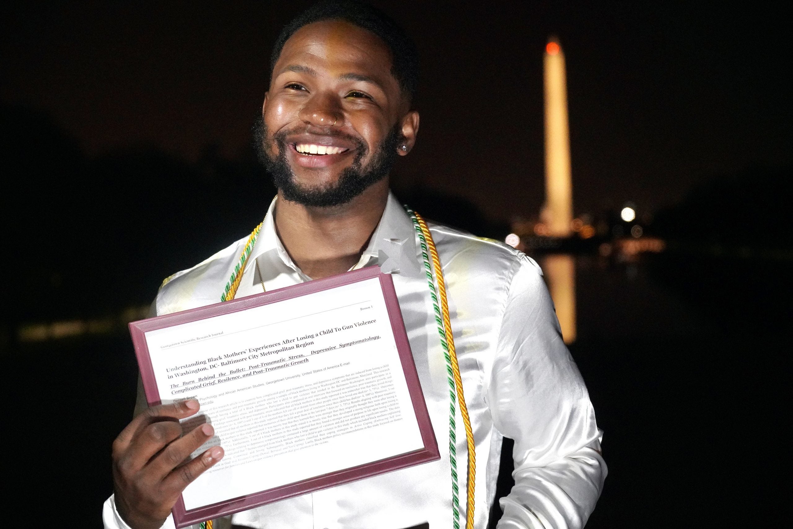 Denzell Brown holds his research in front of Washington Monument at night