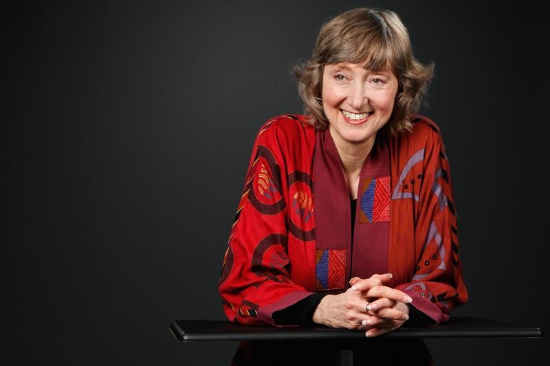 Deborah Tannen wears a red jacket in front of a black background