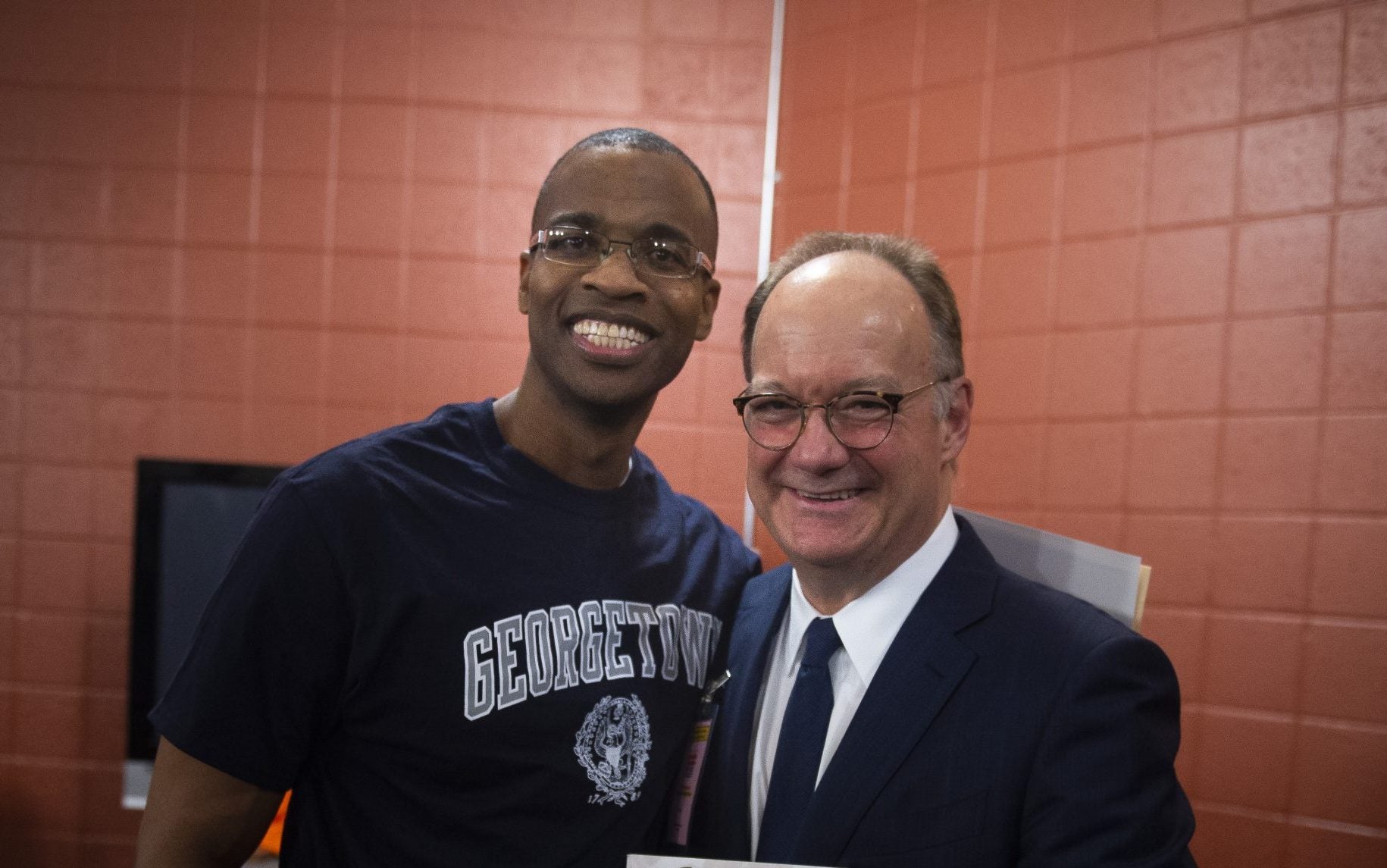 Joel Caston wears a Georgetown shirt and poses with Georgetown President John J. DeGioia