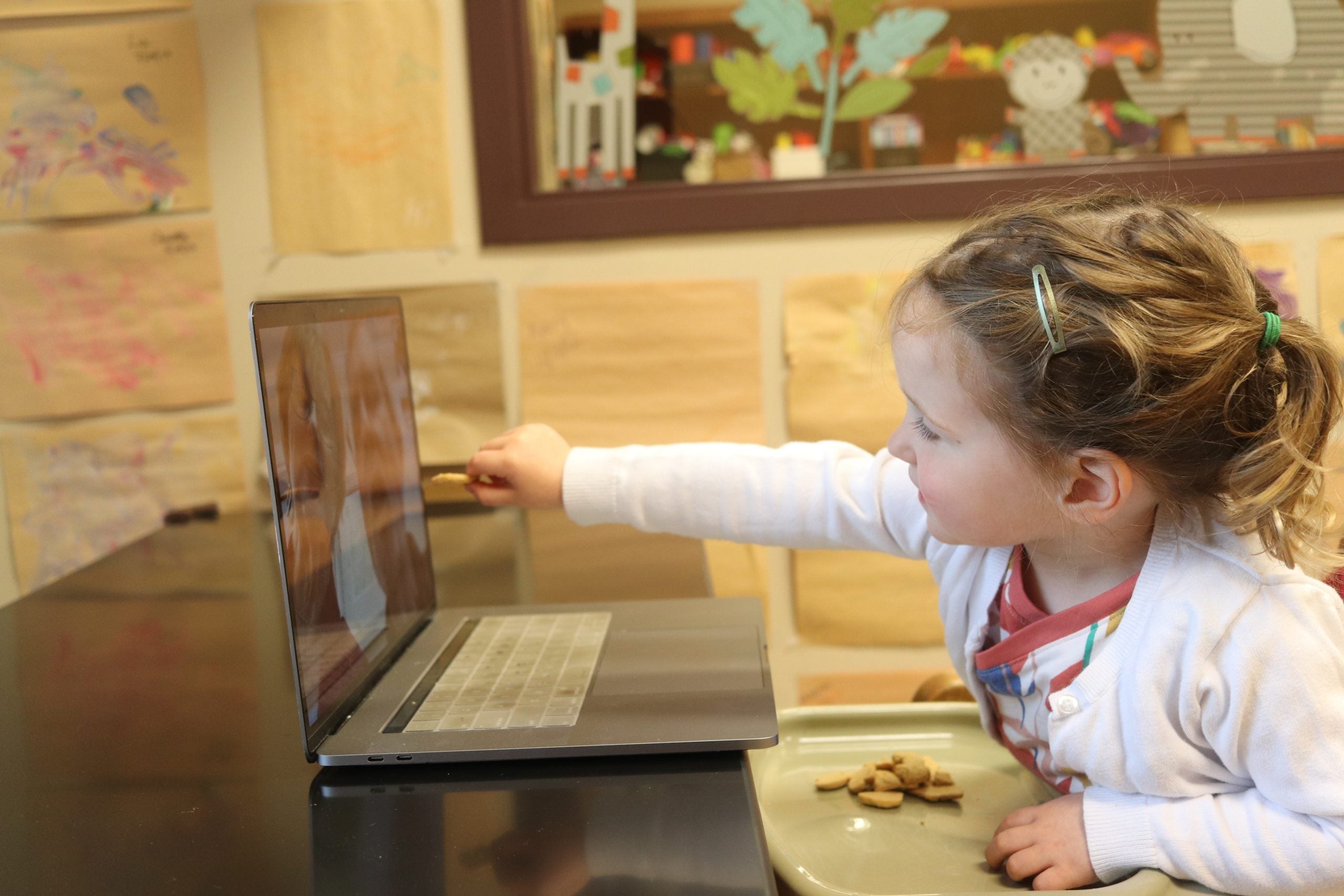 Blonde little girl reaches out to laptop screen