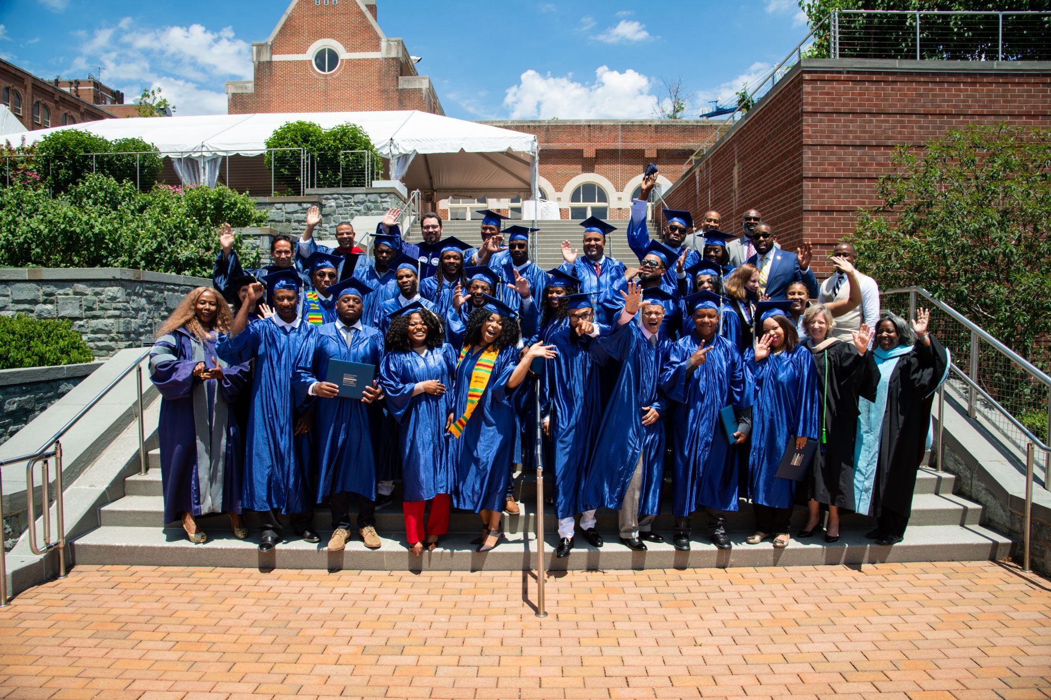 Students in blue graduation robes stand on steps next to Regents Hall