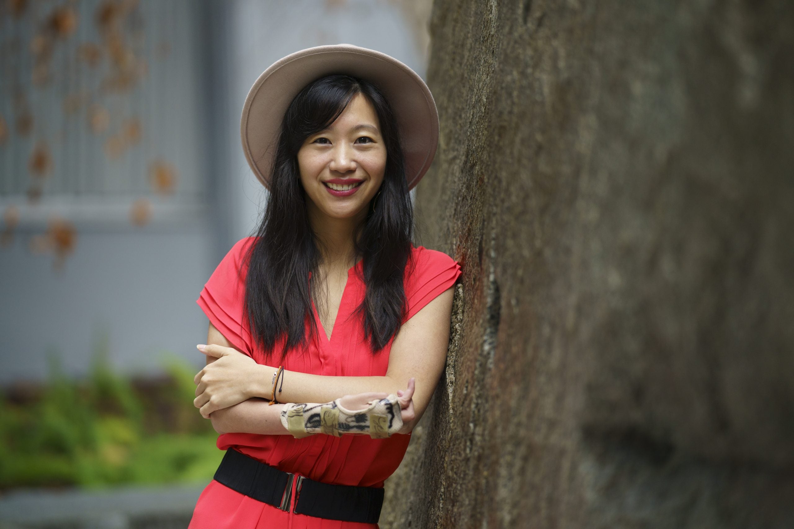 Tiffany Yu wears a hat and pink dress while leaning against a tree